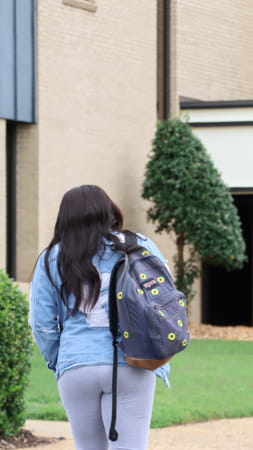 Female student with backpack walking towards the library building