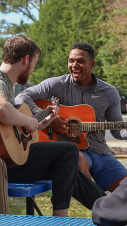 Two male students playing guitar outside