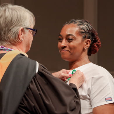 Female nursing graduate receiving her nursing pin from faculty member