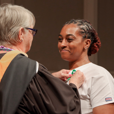 Female nursing graduate receiving her nursing pin from faculty member