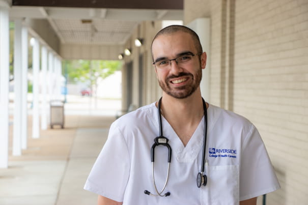 Male student standing under a covered walkway and smiling