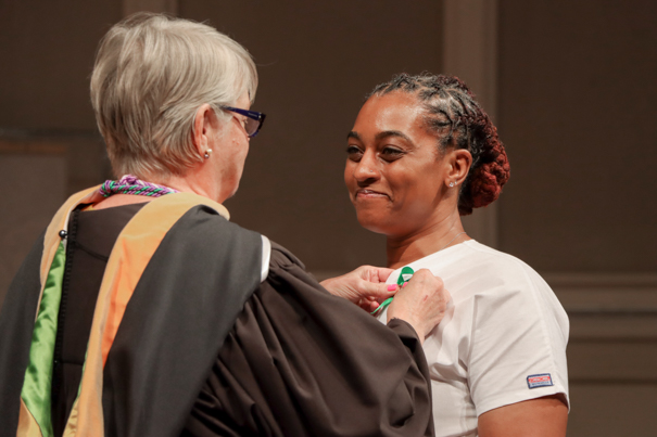 Female faculty member pinning a nurse's pin on a smiling female student’s shirt.