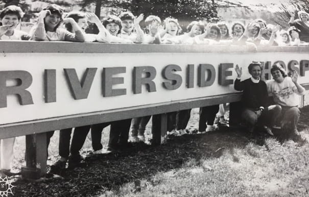 A black and white photo of students in front of an old sign that says 'Riverside Hospital'