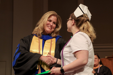 Female faculty member shaking the hand of a female student and handing her a diploma.