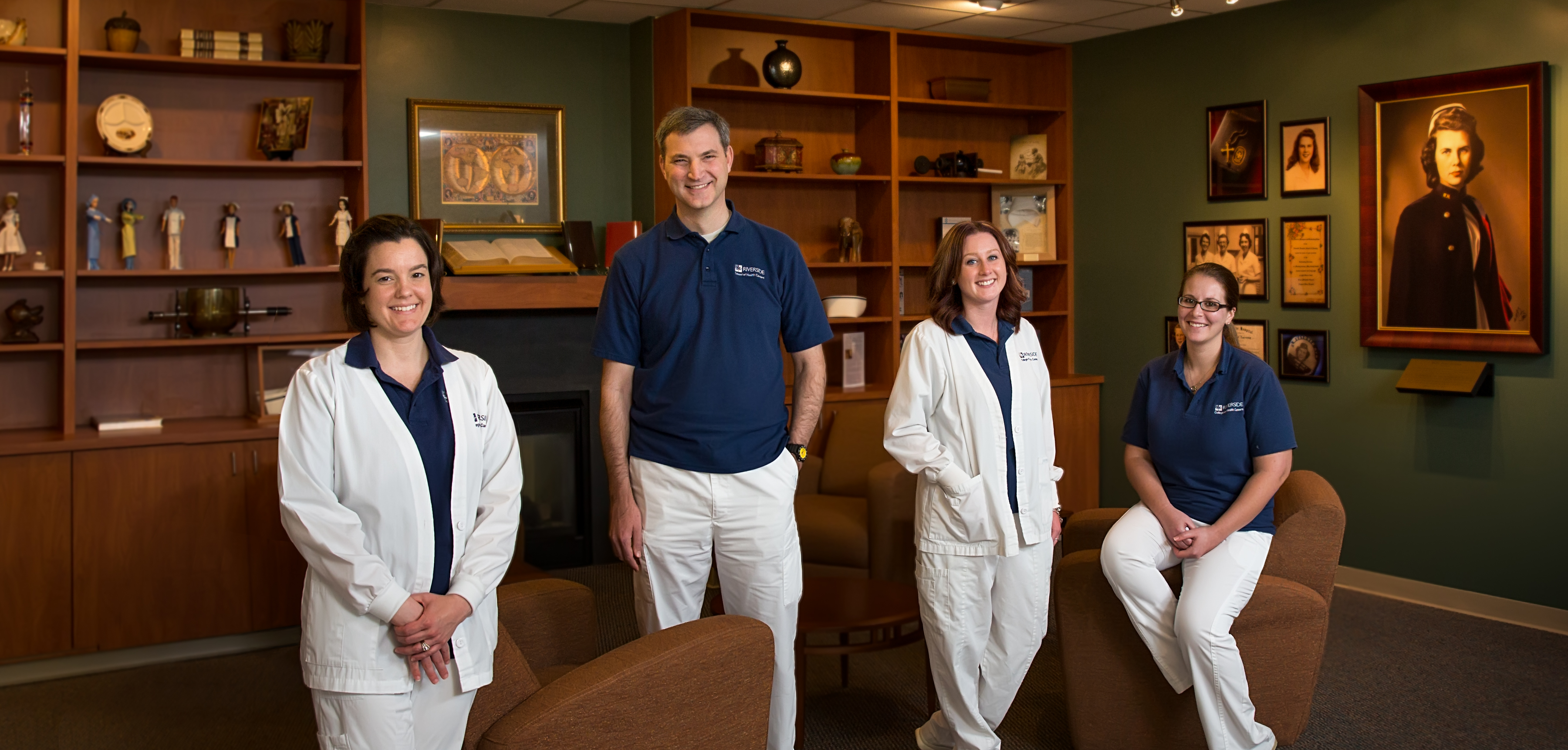 Four students standing in a study lounge room with couches and photos hanging on the walls.
